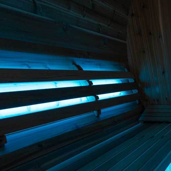 Lighted cedar backrest glowing with blue LED in dark sauna interior for visual ambiance
