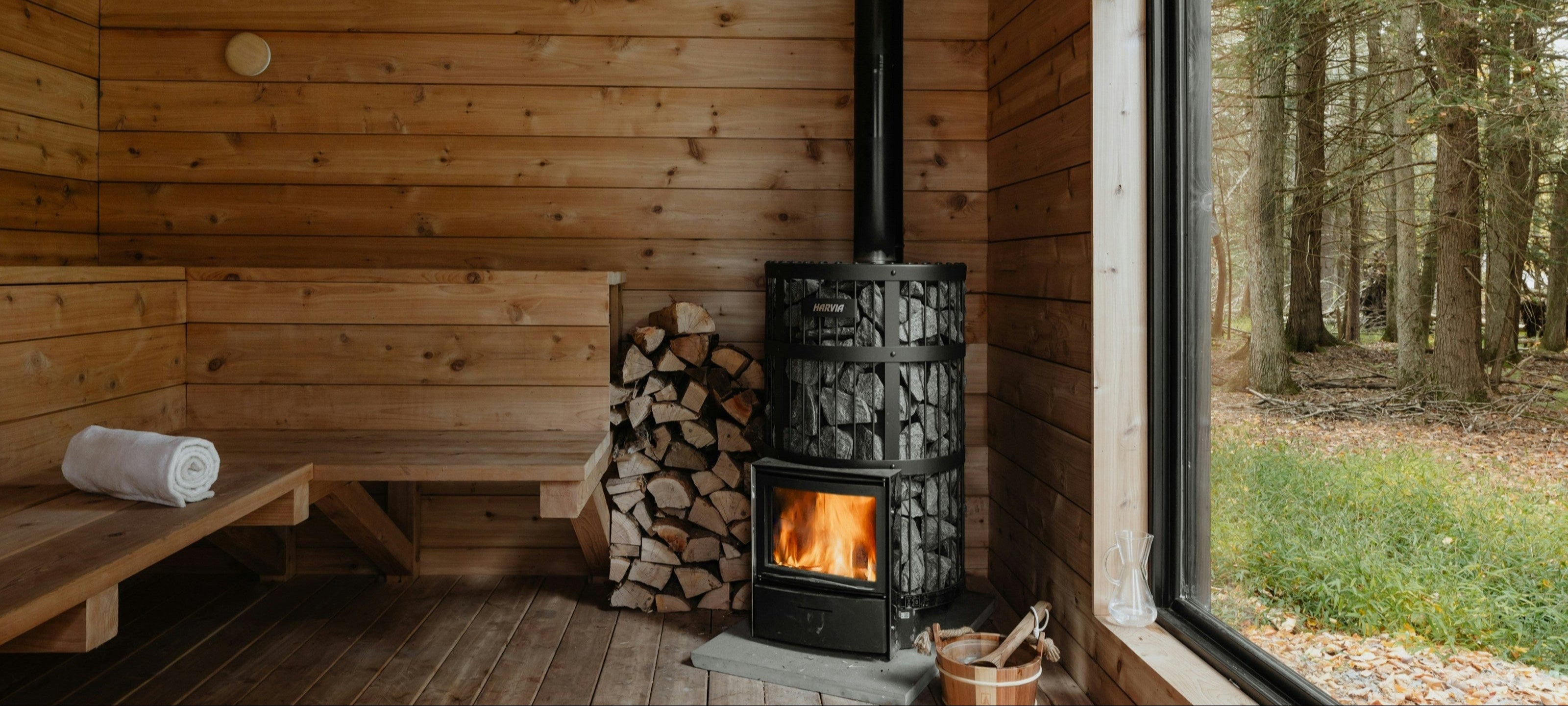 Cozy wood-burning sauna with a panoramic window overlooking a serene forest landscape.