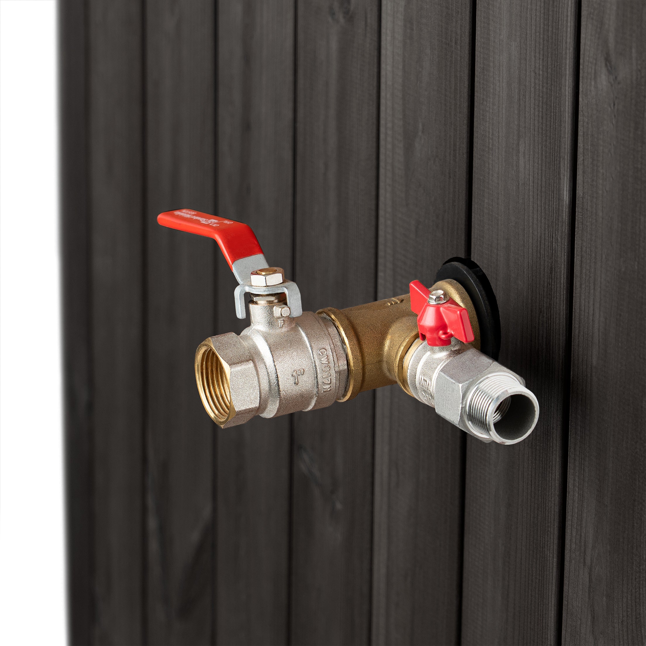 a metallic pipe with two valves attached to it, one of which is red and the other is silver. The pipe is attached to a dark wooden wall.
