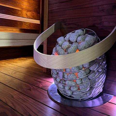 HUUM DROP 6kW Electric Sauna Heater with a polished stainless steel open basket packed with grey sauna stones and a curved rim.